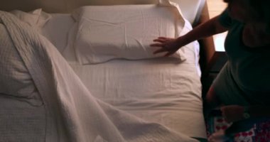 Older woman prepares to go to bed and sleep. Person lays down in bed and turns off night stand besides bed