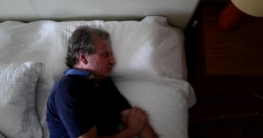 Older man stretching and waking up from afternoon nap, gets out of bed
