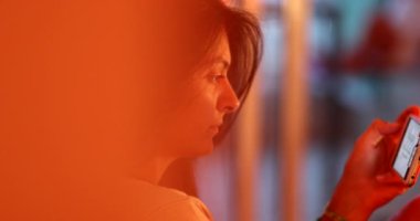 Woman holding cellphone at night sitting in sofa, revealing person, good for transition