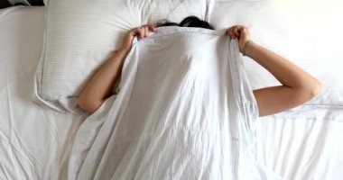 Funny young woman playing hide and seek peekaboo under blanket in bed