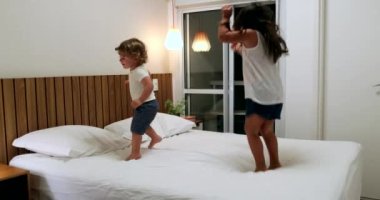 Children jumping up and down on bed. Active happy kids bouncing, little girl and toddler boy
