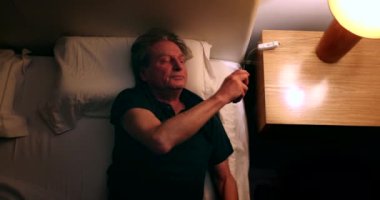 Man turns nightstand light ON and picks up cellphone. Person checking smartphone screen