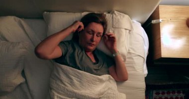 Worried Older woman turning nightstand light ON unable to sleep feeling stressed suffering from insomnia