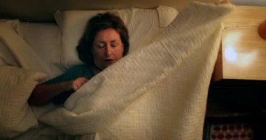 Woman lies in bed resting and relaxing at night, top view