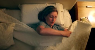 Older woman lying in bed grabbing smartphone and browsing online. Senior using phone before sleep