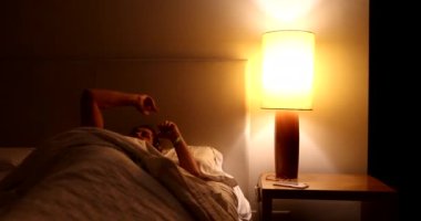 Woman turns lamp light on and gets up from bed at night