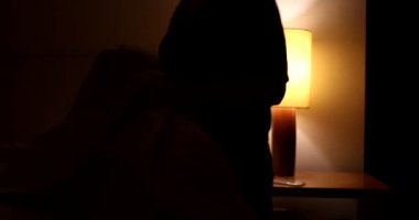 Woman prepares to go to bed and sleep. Person lays down in bed and turns off night stand besides bed