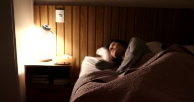 Woman switches nightstand lamp light on and gets out of bed in the night
