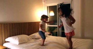 Children jumping up and down on bed. Active happy kids bouncing, little girl and toddler boy