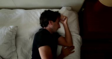 Young man getting up from bed after nap. Person waking up and gets out of bed