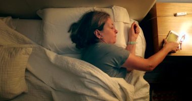 Woman turns on nightstand light and picks up cellphone in the middle of the night