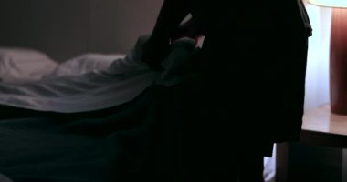 Man prepares to go to bed and sleep. Person lays down in bed and turns off night stand besides bed