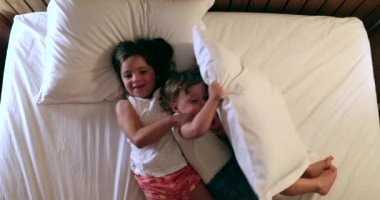 Cute children in bed, little girl and toddler boy playing before sleep. Top view