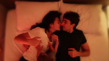 Couple in bed with baby at night. Husband and wife lying down kissing with infant toddler