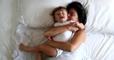 Mother cuddling with baby toddler boy in bed in the morning