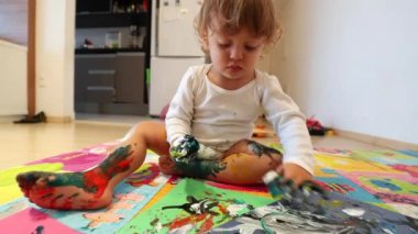Messy toddler baby playing with colorful painting in living-room