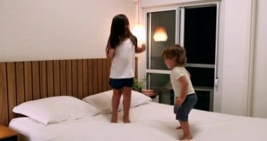 Children jumping up and down on bed. Active happy kids bouncing, little girl and toddler boy