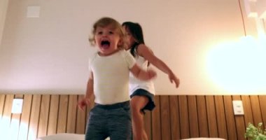 Children bouncing jumping up and down in bed at night. Little girl sister and toddler boy brother having fun