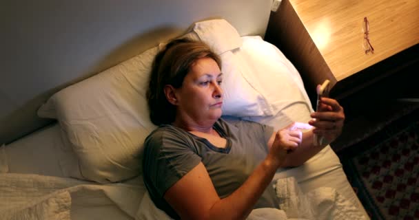 Woman Picks Phone Nightstand Lying Bed Older Lady Browsing Internet — Vídeo de Stock