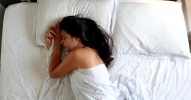 Woman waking up in the morning lying in bed, top view perspective