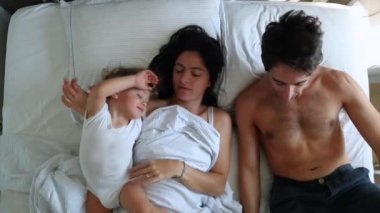 Casual parents in bed with infant baby. Mom and dad in morning bed with toddler. Top view