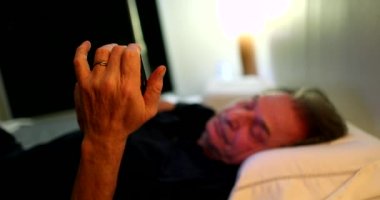 Older man looking at cellphone screen at night laying down in bed
