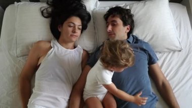 Mother and father lying in bed with crying baby. Upset infant, top view