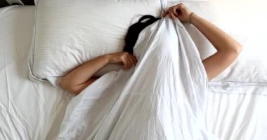 Fun young woman playing peekaboo with bed blanket. Girl gide and seek in the morning