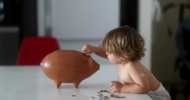 Adorable baby boy adding savings inside piggy bank