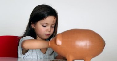 Little girl adding coins inside piggy bank. Child saving money concept