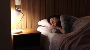 Woman turning bedside lamp on in the middle of the night. Girl gets out of bed