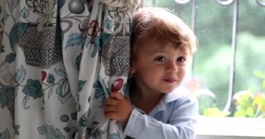 Toddler boy hiding behind curtains. Happy child plays hide and seek
