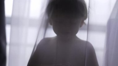 Cute baby toddler standing behind curtain cloth looking at camera