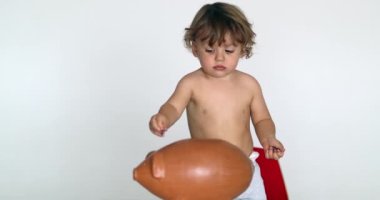 Toddler boy saving money inserting coins inside piggy bank