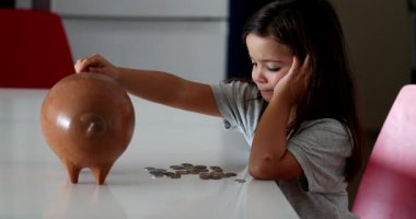 Little girl adding coins inside piggy bank. Child saving money concept