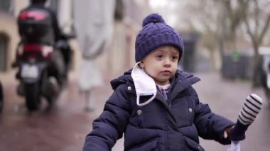 Little two year old toddler walking in city sidewalk during winter