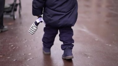 Little toddler walking outside on sidewalk during winter time in city