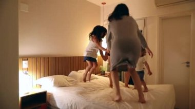 Aile yatakta hoplayıp zıplıyor. Kız kardeşler ve çocuklar birlikte oynuyorlar.