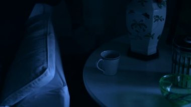 Man switching table light ON and grabbing cup of tea sea relaxing on sofa