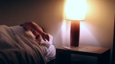 Older woman waking up in the middle of the night suffering from insomnia. Person turning bedside lamp on