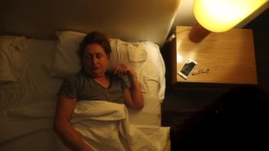 Older woman waking up in the middle of the night, person turning night lamp on and getting out of bed