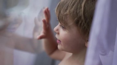 Child standing by window glass pointing with finger, toddler 2 year old baby