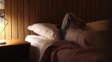 Woman turning bedside night lamp OFF. Perosn in bed going to sleep