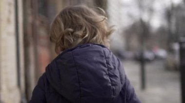 Back of toddler walking in city sidewalk during winter