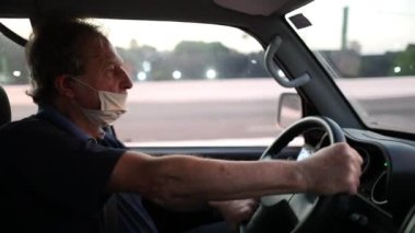 Older man looking at rear view mirror while driving and wearing covid-19 face mask