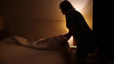 Woman prepares to go to bed and sleep. Person lays down in bed and turns off night stand besides bed