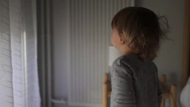Little toddler closing automatic blinds, kid watching blinds go down