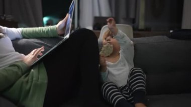 Mother in front of laptop at night sitting in sofa with infant
