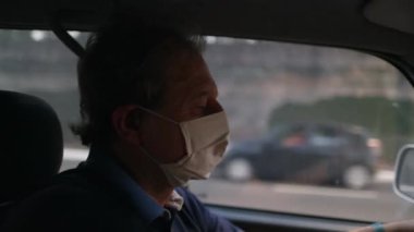 Older man driving car while wearing covid-19 face mask