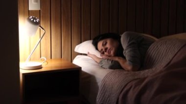 Woman lies in bed thinking before going to sleep. Person turning bedside lamp off